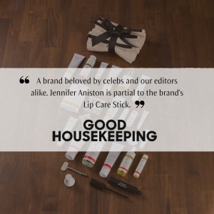 Good Housekeeping promotional flat lay of beauty products, cosmetics tubes, a canvas pouch and quote text on a wooden table.