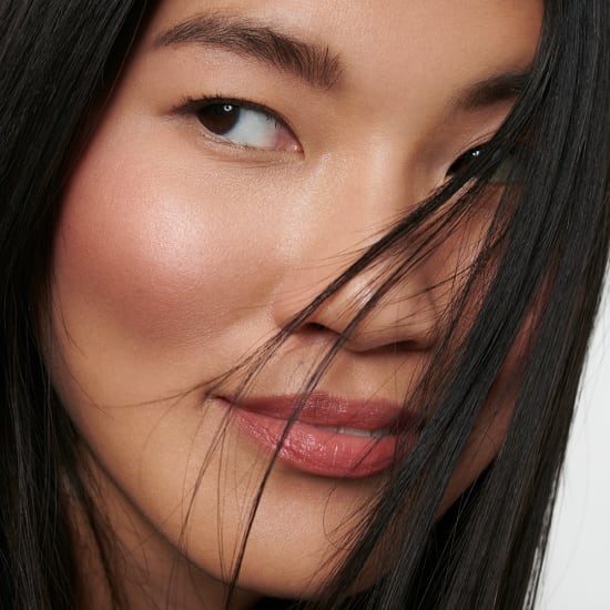 Close-up of a woman's face with glossy lips, glowing skin and dark hair partly covering one eye.