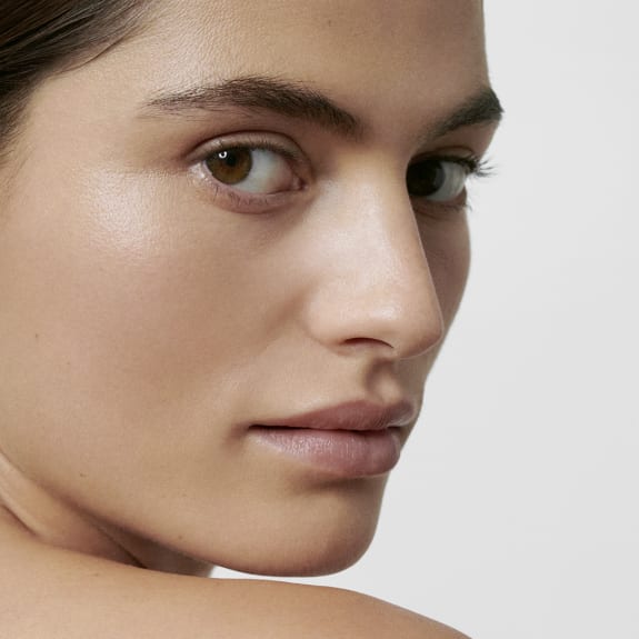 Close-up of a woman’s face with natural skin and minimal makeup, looking over her shoulder.
