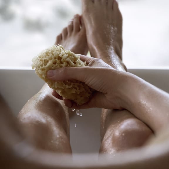 Hand scrubbing wet feet in a bathtub with a sponge, showing home foot care.