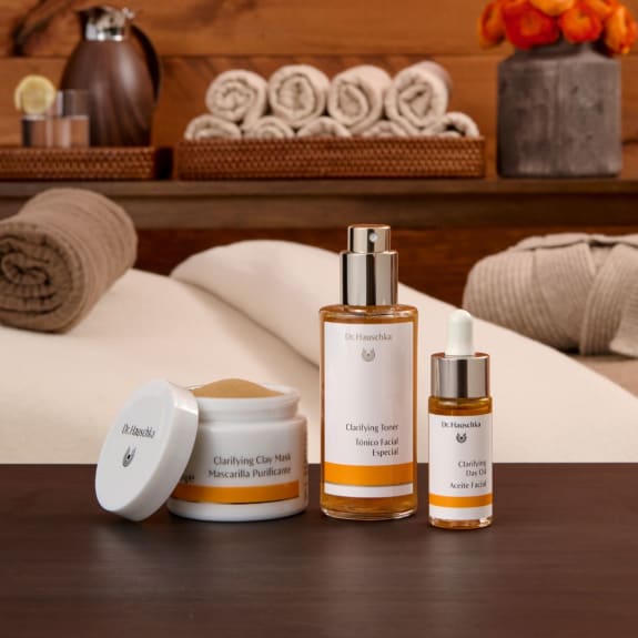 Spa-style display of Dr. Hauschka clarifying skincare products on a wooden table, with rolled towels and soft lighting.