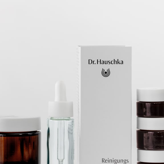 Dr. Hauschka skincare products in brown jars and a dropper bottle beside a white box on a plain background.