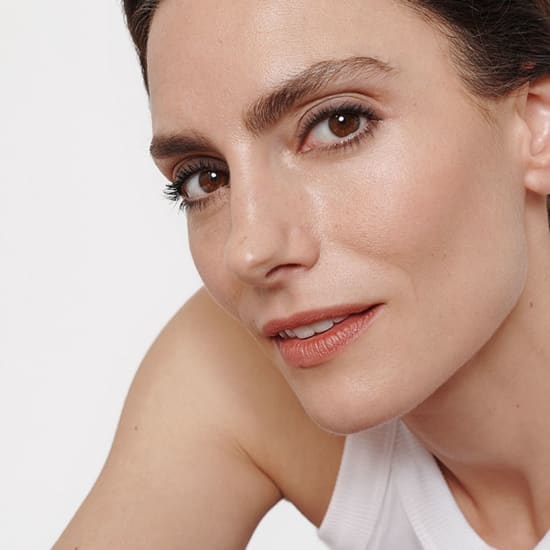 Close-up portrait of a woman with natural makeup, looking at the camera against a plain white background.