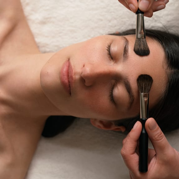 A woman lying down with two brushes above her forehead.