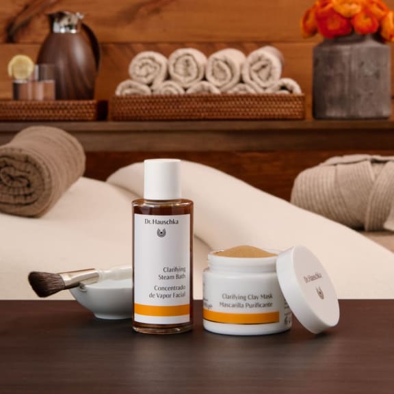 Skincare products on a spa table: clarifying steam bath bottle, clay mask jar, brush and towels.