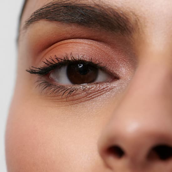 Close-up of one eye with shimmery peach eyeshadow, winged mascara and a neatly groomed eyebrow.