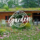Wildflower garden in bloom beside a timber building with a living roof and 'The Giving Garden' logo overlaid.