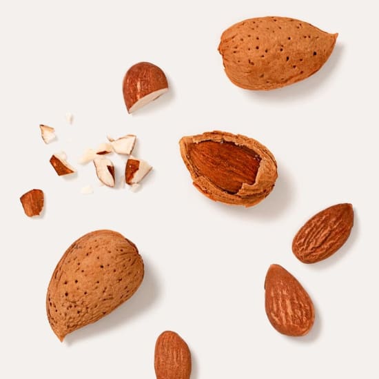 Scattered whole and cracked almonds on a white background, with a few broken shell pieces.