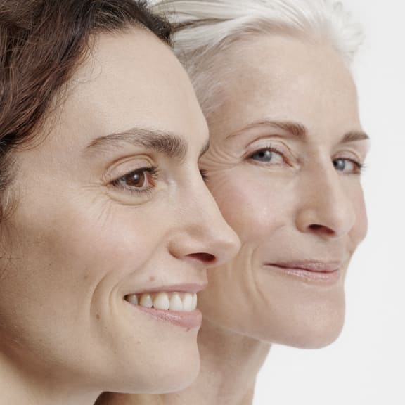 Two women in profile, one younger and one older, smiling softly against a white background.