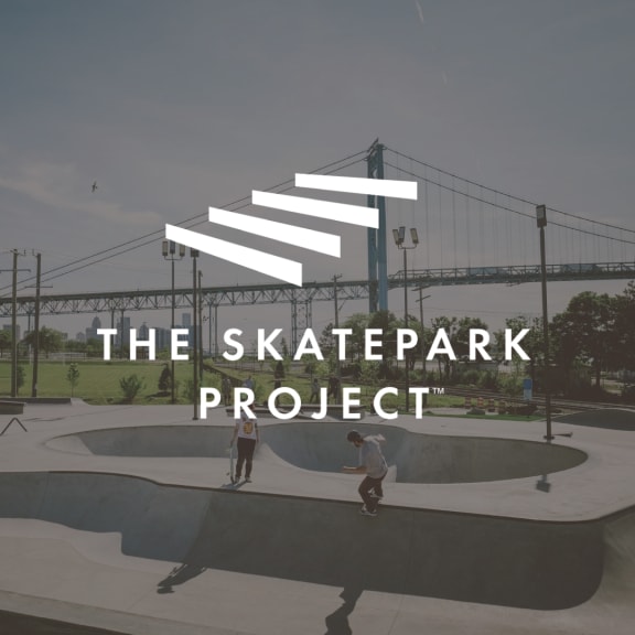 The Skatepark Project logo over a skatepark with skaters and a suspension bridge in the background.