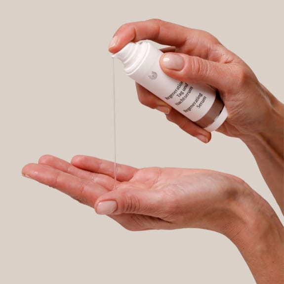 Hands pouring clear serum from a white bottle into an open palm against a plain beige background.