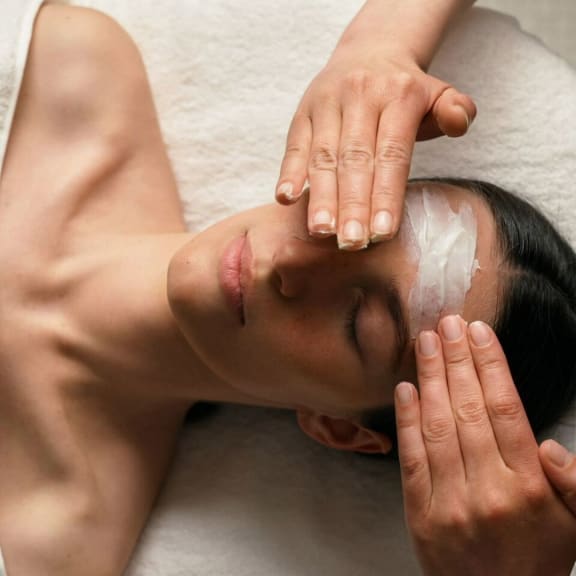 Spa facial treatment with a woman lying down, eyes closed, while hands apply cream to her forehead.
