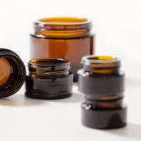 Several amber glass jars in different sizes on a white background, one tipped on its side in the foreground.