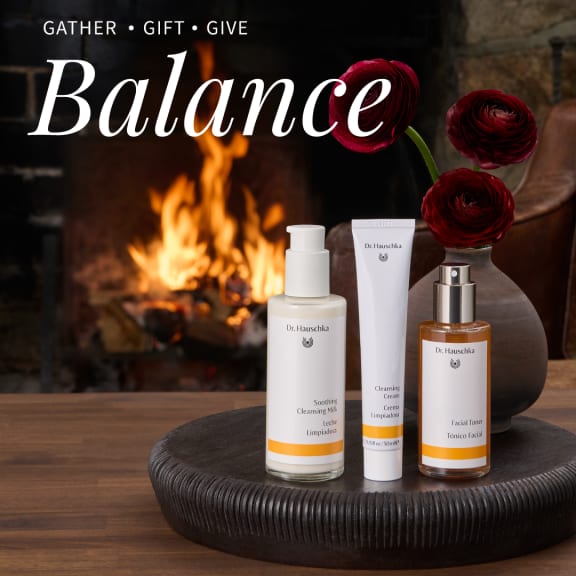 Dr. Hauschka Cleanse Tone gift set on a wooden tray before a fireplace, with red flowers and the word Balance.