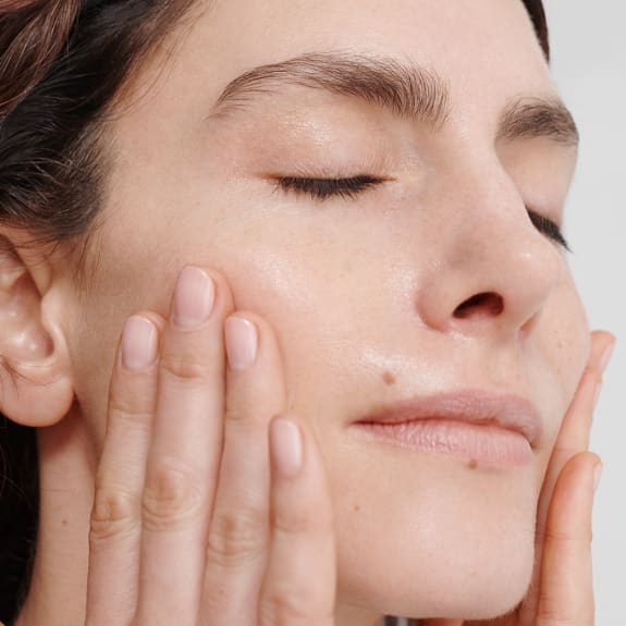 Close-up of a woman gently pressing moisturizer into her cheeks with closed eyes.