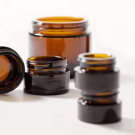 Several amber glass jars in different sizes on a white background, one tipped on its side in the foreground.
