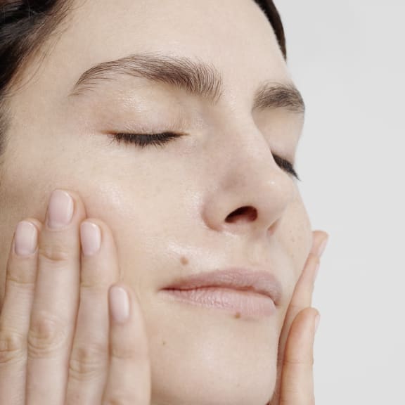 Close-up of a woman with eyes closed, gently pressing her cheeks with both hands.