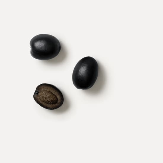 Three black olives on a white background, one cut open to show the pit.