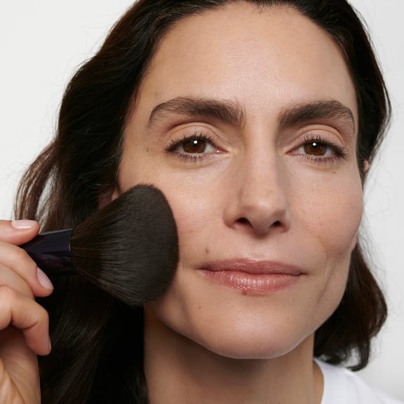 Close-up of a woman applying face powder with a large makeup brush.