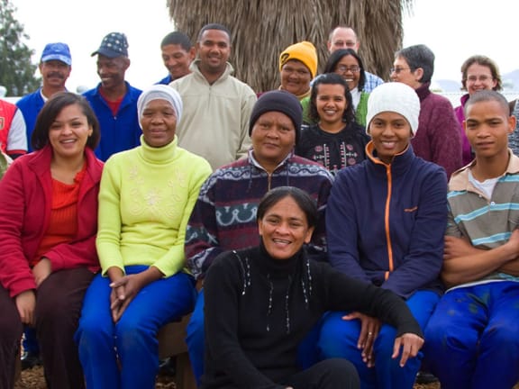 A diverse group of people sit and stand together outdoors, smiling at the camera.