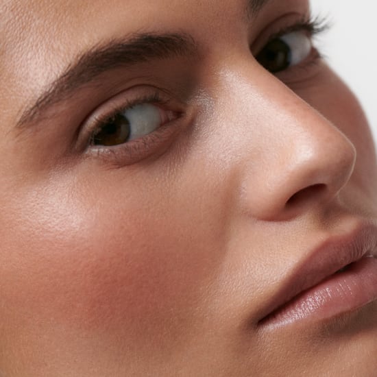 Close-up of a woman's face with natural skin texture, looking sideways with a soft, no-makeup look.