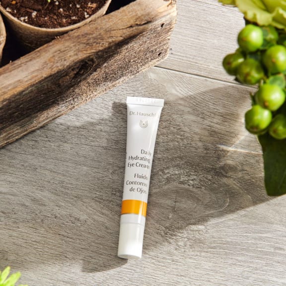Tube of Dr. Hauschka Daily Hydrating Eye Cream on a wooden surface with plants.