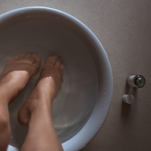 Feet soaking in a white basin of water beside a small bottle and cap on a countertop.