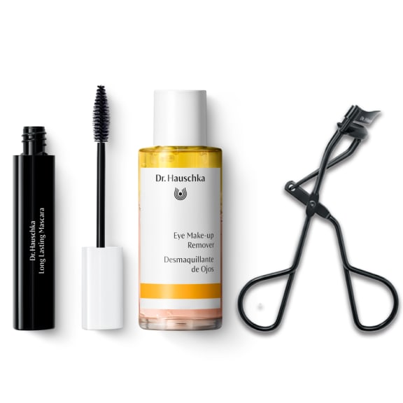 Dr. Hauschka beauty set on white: mascara tube and wand, eye makeup remover bottle, and eyelash curler.
