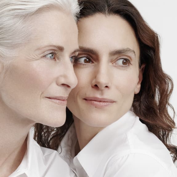Close-up of two women in white shirts, one older and one younger, leaning together and looking off to the side.