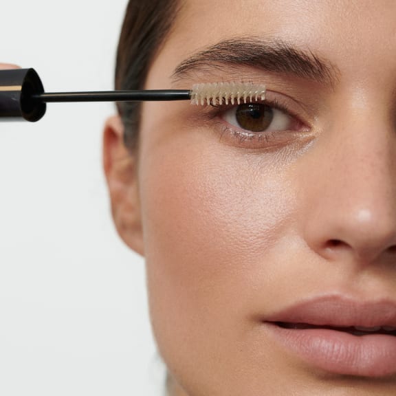 Close-up of a person applying clear mascara to their upper eyelashes with a wand.