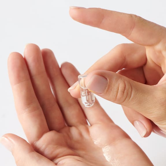 Hands holding a small clear ampoule above an open palm against a white background.