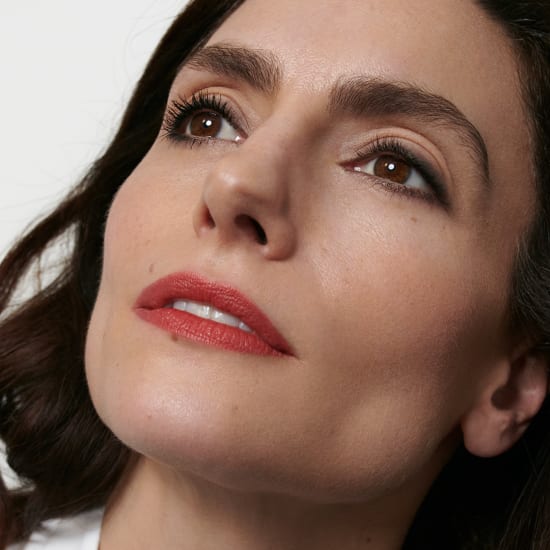 Close-up portrait of a woman with smoky eye makeup, red lipstick, and a soft upward gaze.