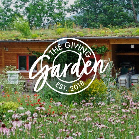Wildflower garden in bloom beside a timber building with a living roof and 'The Giving Garden' logo overlaid.