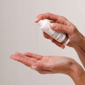 Hands dispensing clear serum from a white pump bottle into an open palm.