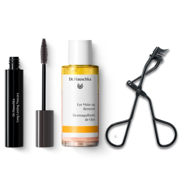 Mascara tube with wand, eye makeup remover bottle and eyelash curler on a white background.