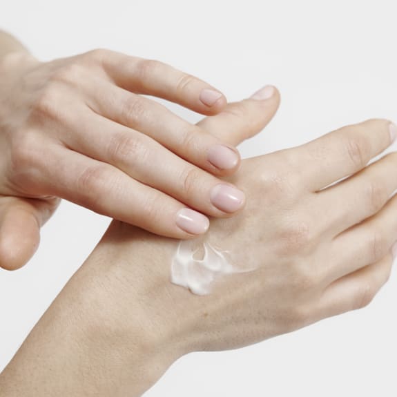 Close-up of hands applying white lotion to the back of a hand.