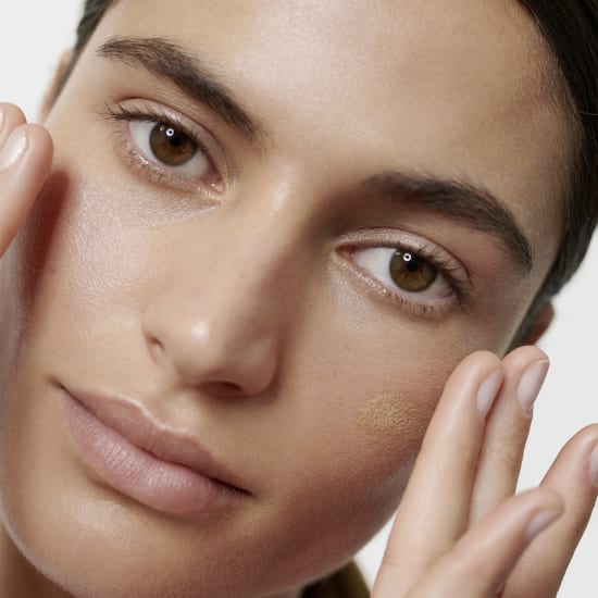 Close-up of a woman’s face applying foundation to her cheek with her fingers.